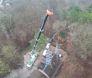 BMS-mobilkran med langt udlæg arbejder ved en telemast omgivet af skov, set fra luften