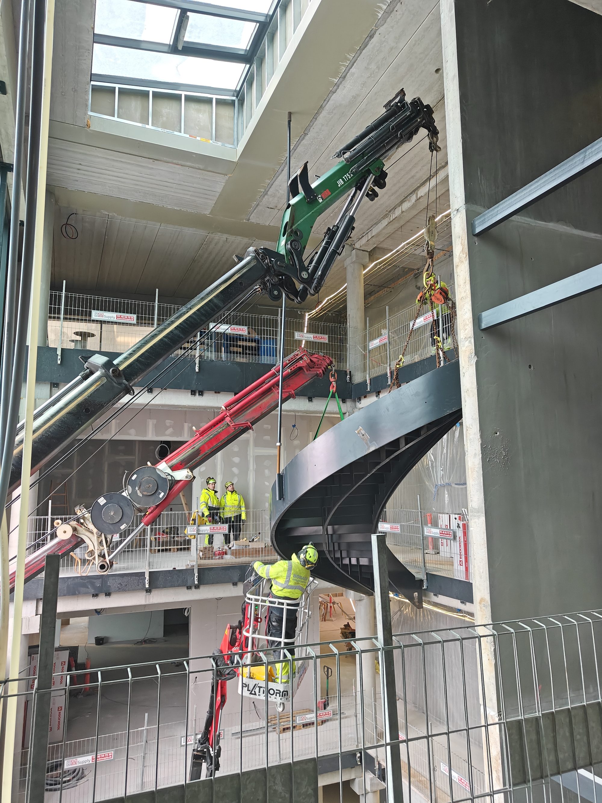 kraner sænker en buet sort stål-trappe på plads i et atrium 