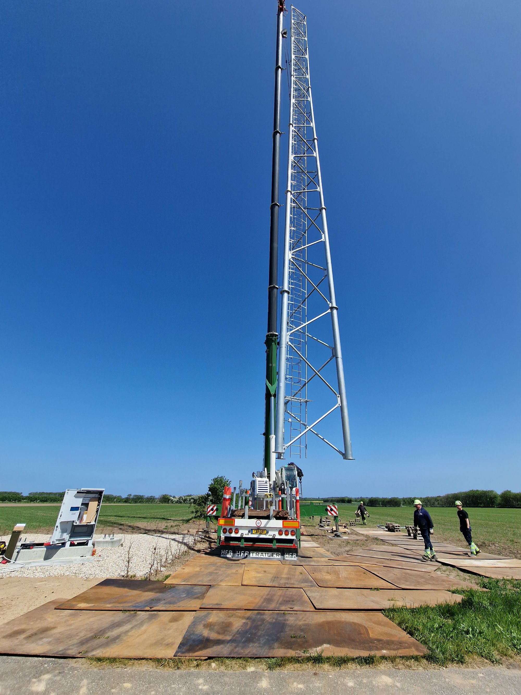 Fuldrejst telemast i markareal med mobilkran ved siden af
