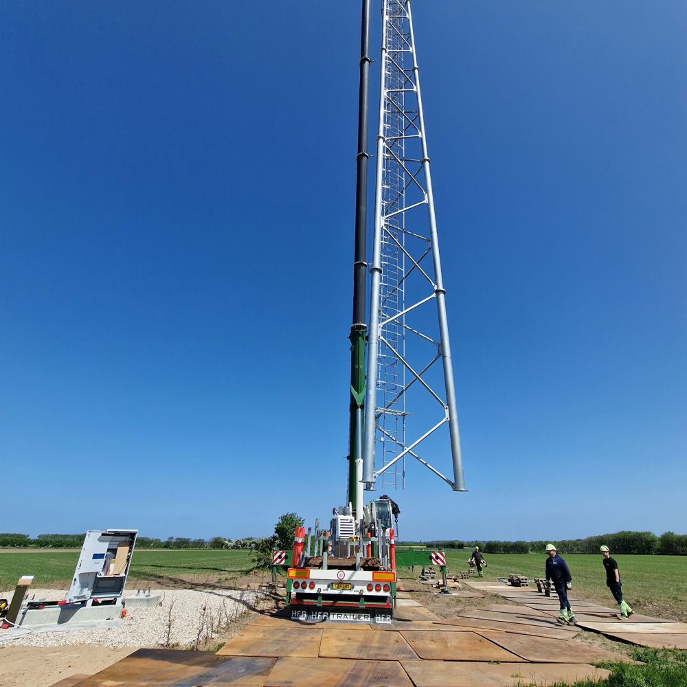 Fuldrejst telemast i markareal med mobilkran ved siden af