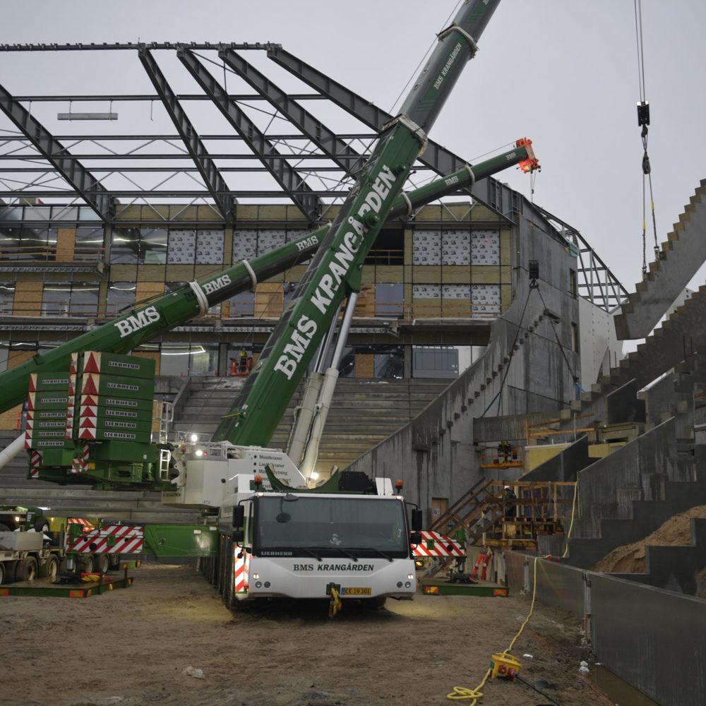 To BMS Krangården-kraner løfter et præfabrikeret betontrappeelement på plads under opførelse af et stadion