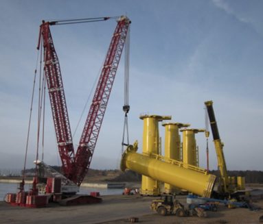 Kran løfter gult transition piece ved havnen i Lubmin