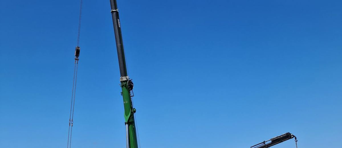 Mobilkran og lastbilkran hejser en telemast i et markareal