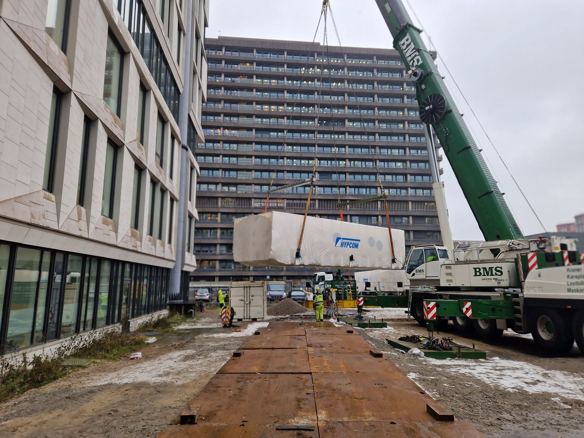 Mobilkran hejser stort trykkammer op mellem højhuse ved Rigshospitalet