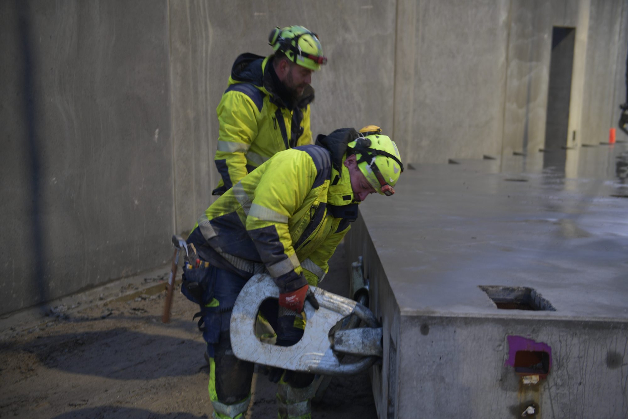 To BMS-riggere fastgør en krankrog til et betonelement på en byggeplads