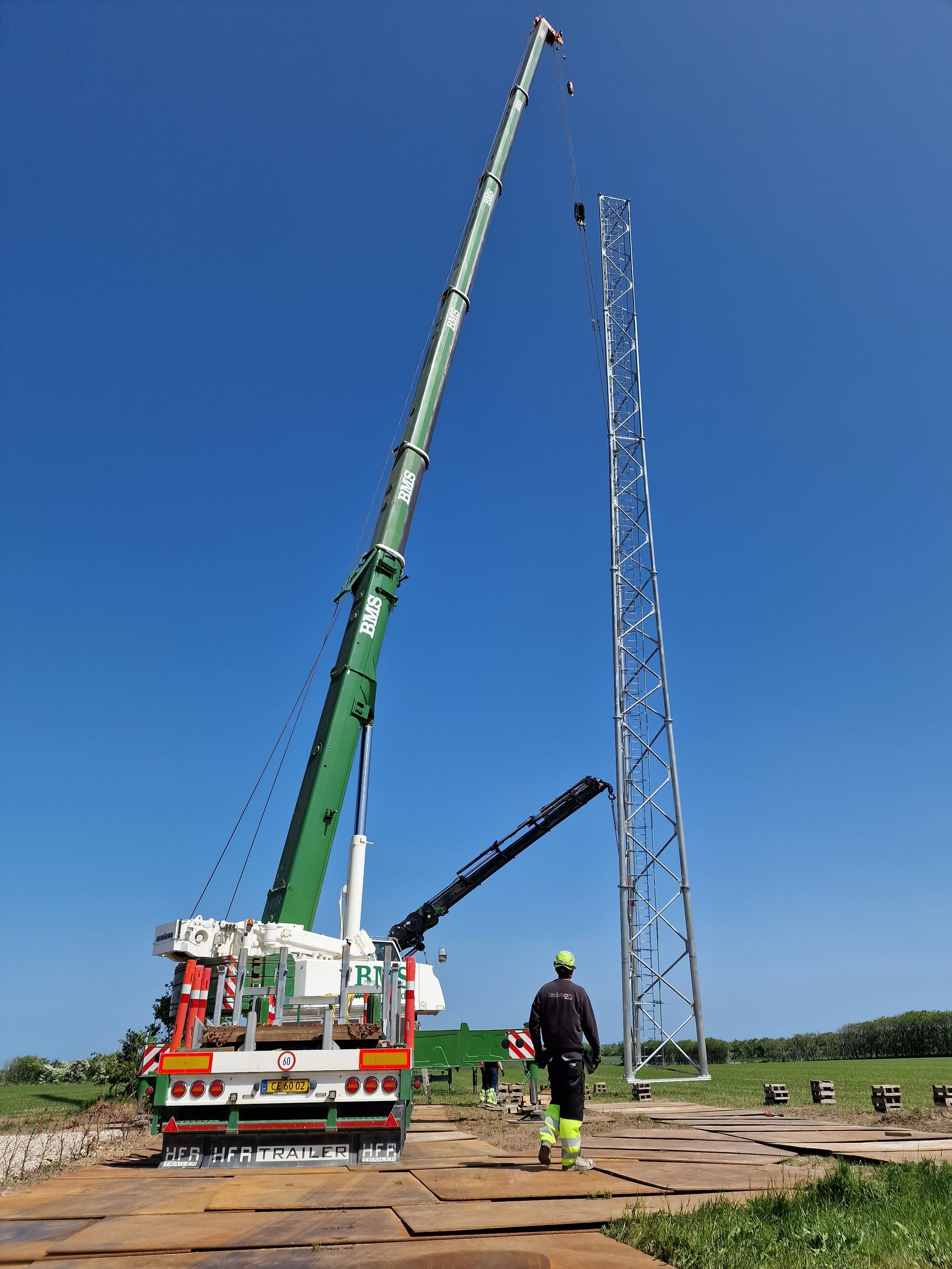 Fuldrejst telemast i markareal, mobilkran og to medarbejdere ved siden af